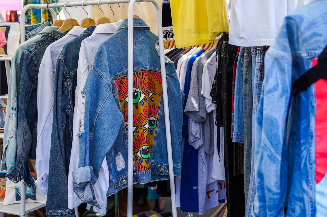 Colorful denim jackets and shirts hanging on a rack at a vibrant flea market.